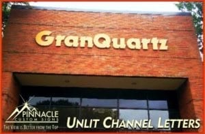 Exterior view of a brick building with the business name 'GranQuartz' displayed in unlit channel letters. The sign is mounted above large windows. The Pinnacle Custom Signs logo and tagline 'The View is Better from the Top' are in the bottom left corner of the image.