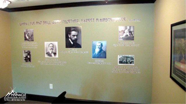 Interior wall decorated with decals featuring historical figures and quotes, along with the phrase 'When love and skill work together, expect a masterpiece' at the top, displayed in a room with light green walls and black trim